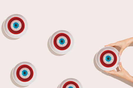 Female hands holds bowl of dark red jelly with eyeballs. Isolated pastel beige background. Abstract funny Halloween holiday concept. Minimal flat lay.の写真素材