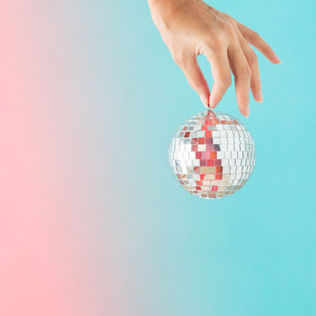 Minimal abstract Xmas card with female hand holding disco ball on isolated iridescent turquoise-pink background. New Year's Eve holiday entertainment concept. Christmas decoration.の写真素材