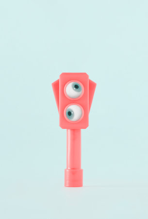 Pink semaphore with eyes looking around on isolated pastel background. Minimal creative abstract surreal concept of surveillance, observation or monitoring. Idea of urban control.の写真素材