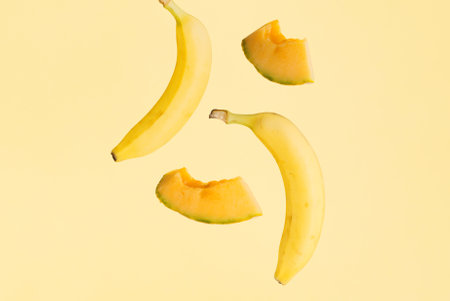 Bananas and melon slices hover over isolated pastel yellow background. Minimal creative concept of tropical summer fruit. The idea of raw food diet rich in potassium.の写真素材