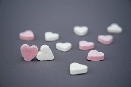 Two candy hearts togther, with multiple other candy hearts spread around on a grey background