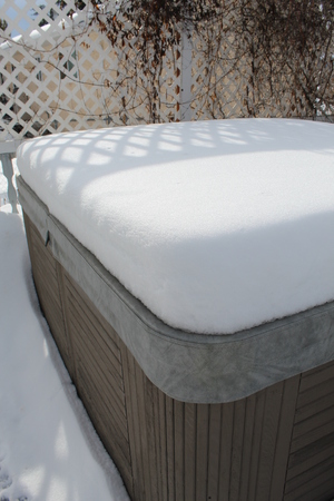 Closeup of snow covered hot tub with sun and shadows. Trellis and vines in background.の写真素材