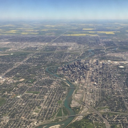 Aerial view of downtown Calgary Alberta in summer with river, streets and buildings. Yellow canola fields with haze and horizon in background.の写真素材