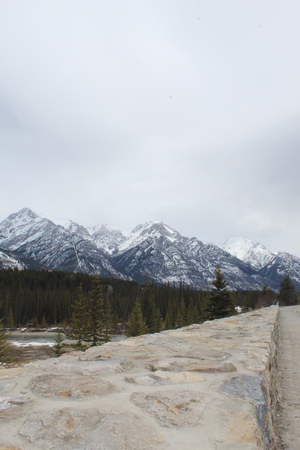 Closeup of rock and cement wall with forest and snow capped mountains in background. Cloudy snowy sky over mountains.の写真素材