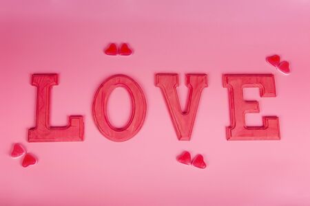 Word love in fuxia wooden letters with jelly beans hearts on pink background. Selective focus. Valentine, love concept.の写真素材