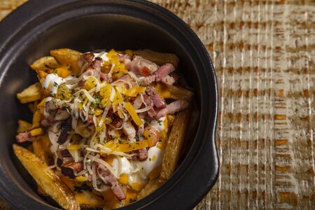 Casserole of rustic french fries with bacon and cheese on wooden background. Isolated image with...