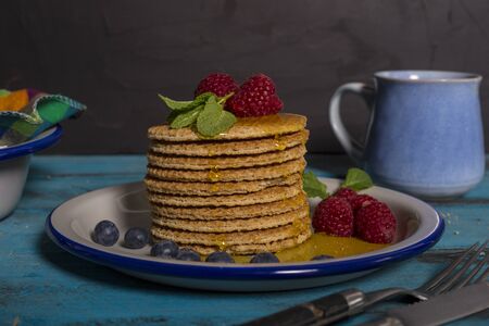 Close-up of a stack of Dutch waffles with raspberries, blueberries and honey on blue wooden...