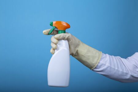 Hand with rubber glove holding a white spray bottle on blue backgroundの写真素材