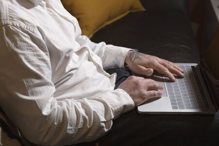 Closed shot of man working with laptop on sofa at home. Telework space on the sofa at home. Telework conceptの写真素材