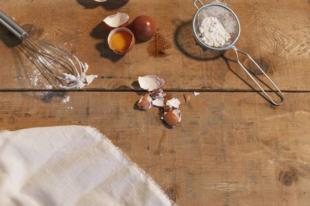 Ingredients for the dough: eggs and flour with a whisk on wooden background and kitchen cloth. Top...