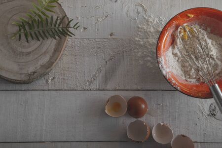 ingredients and tools to make the dough, flour, eggs and a whisk on a white wooden bottom. isolated...