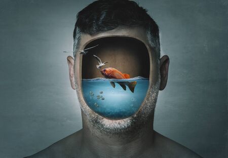 Surreal portrait of man with cropped face filled with water with a fish inside on a blue background. Surreal image. Surrealism.の写真素材