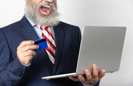 Excited mature man in suit holding a credit card using online laptop purchase. Senior man with...