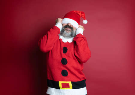 Caucasian bearded man with Santa Claus is too big a hat for him. Isolated on red backgroundの写真素材