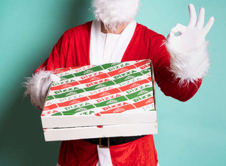 Closed portrait of Santa Claus holding a pizza box and giving ok with his hand on blue background