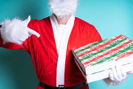Closed portrait of Santa Claus pointing a finger at a pizza box on blue backgroundの写真素材