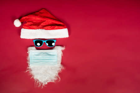 Santa Claus head with surgical mask, hat, white beard and sunglasses with copy space for text on red background.の写真素材