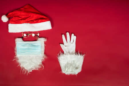 Santa Claus head with surgical mask, hat, white beard and gloves with copy space on red background.の写真素材