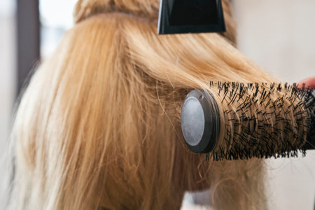 Hairdresser cuts and combs and straightens hair with blow dryer to blonde lady
