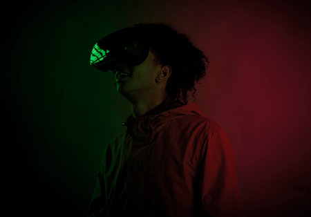 Handsome young afro man smiling with virtual reality headset in studio and colorful lighting. High-tech glasses for virtual reality.の写真素材