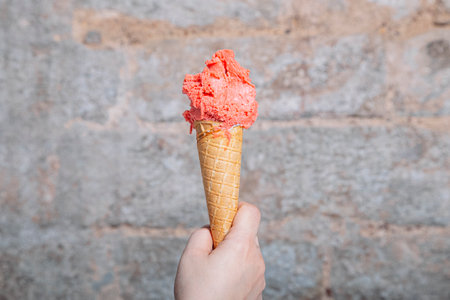 Hand holding strawberry flavor artisan ice cream cone. Strawberry ice cream served in a waffle cone....