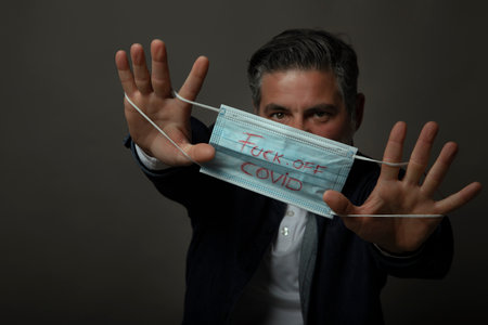 Caucasian man is dissatisfied with the mask regime, the medical mask says "fuck off covid" "の写真素材