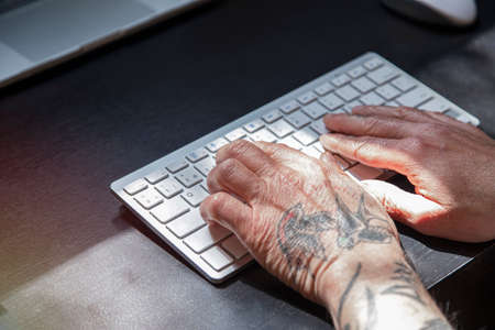 Tattooed hands working on a laptop. Modern businessman typing on keyboard while working in office.の写真素材