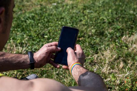 Man with gay flag bracelet holding a smart phoneの写真素材