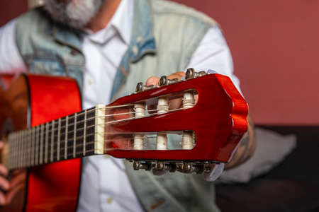 Man adjusting the nodes of the guitar while sitting on the sofa.の写真素材