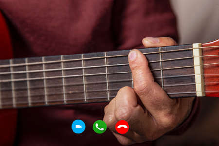 Man giving acoustic guitar lessons while on a video call.