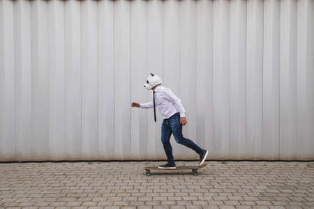 Businessman skateboarding on longboard with a panda bear mask against gray wall