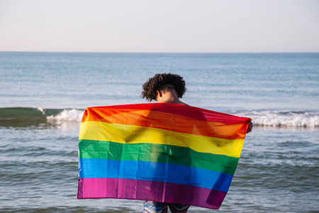 Young latin man with a lgtbi flag on the beachの写真素材