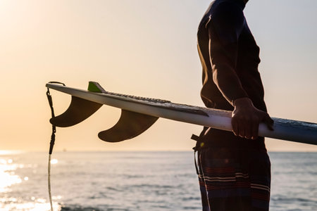 Unrecognizable surfer preparing to surf on the beach at sunriseの写真素材