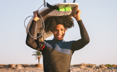 Happy mixed race surfer boy balancing a surfboard on his head. Looking directly at the camera and smiling.の写真素材