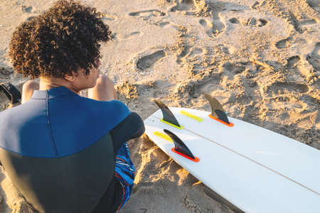 Portrait of young mixed race surfer sitting back to camera.