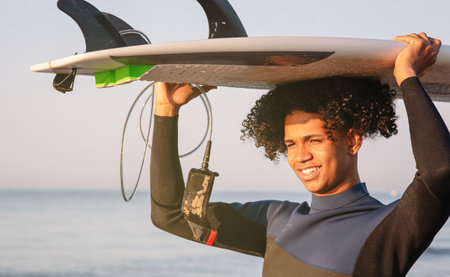 Young Latino surfers carrying surfboard on head with sea in background. A cheerful young afro. Extreme water sport concept. Summer vacation idea. Sunny dayの写真素材