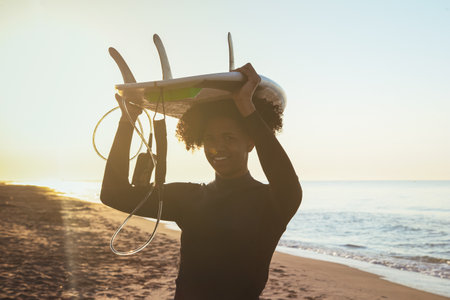 Young Latino surfers carrying surfboard on head with sea in background. A cheerful young afro. Extreme water sport concept. Summer vacation idea. Sunny dayの写真素材
