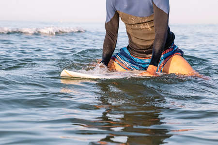 Surfer sitting on his surfboard in the ocean water. The concept of adventure and freedom doing...