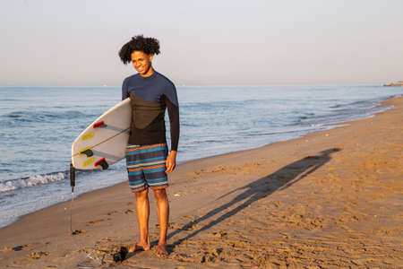 Photo of a smiling young surfer with a surfboard on the beach.の写真素材