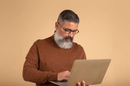 picture of handsome bearded man on light isolated wall background using laptopの写真素材