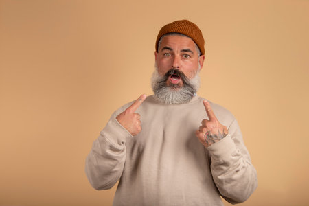 Hipster man looking disappointedly at camera pointing at himself with hands being surprised to be...