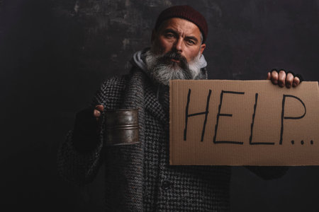 A poor homeless man with placard and a pot for alms on a dark backgroundの写真素材
