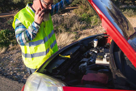 Hispanic talking on the phone to ask a mechanic to come fix his broken down car on the road