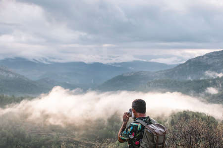Rear view of man drinking coffee while contemplating landscape on mountainの写真素材