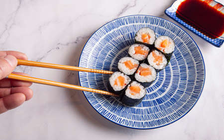 Maki rolls with salmon. The man's hand holds a roll with chopsticks.の写真素材