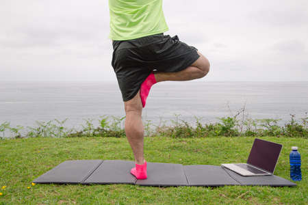 Close up of a man practicing body balance while doing a treetop yoga pose on the beach at sunset