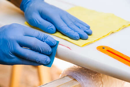 Surfer with protective gloves sanding a repair on the surfboard.の写真素材