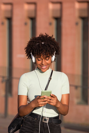 Smiling latin american woman with headphones listens to music on smartphoneの写真素材