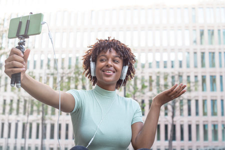 Young afro-haired student sitting on the campus stairs on a video call with her relativesの写真素材