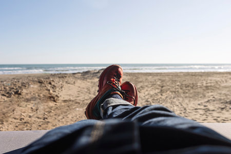 Man's legs in blue jeans and hiking shoes lying inside a van on the beach. Loneliness man tourist...